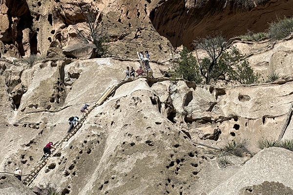 Visitors climb ladders to ancient cliffside dwellings at Bandelier National Monument.