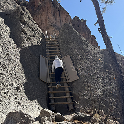 Visitors climb ladders to ancient cliffside dwellings at Bandelier National Monument.