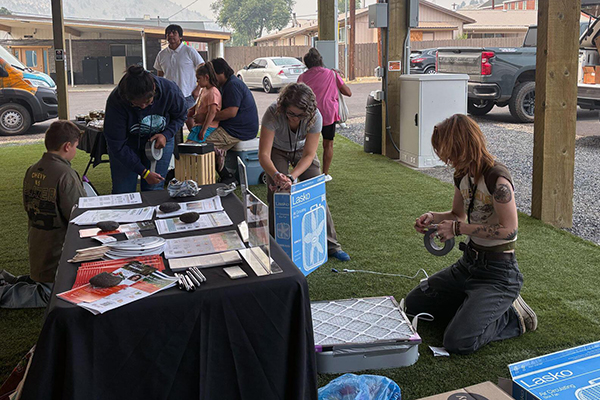 Ariel Cowan (background, middle) and Jenna Deibel (far right) assemble box fan air filters at the Thursday outdoor market in Warm Springs.
